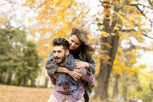 Young Man Giving Young Woman Piggyback Ride Amongst Autumn Trees