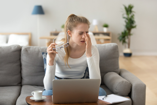 Young woman suffering from dry eyes while rubbing eyes and removing glasses