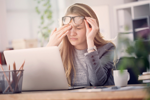 Young woman rubbing painful eyes while trying to use laptop