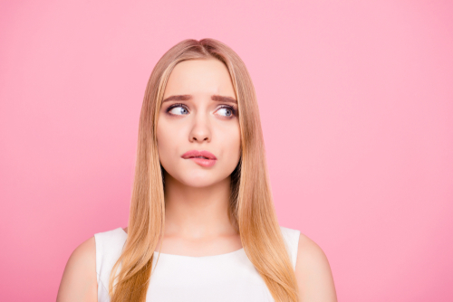 Young woman with concerned expression on pink background