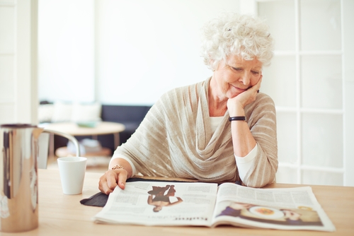 Smiling older woman reading a magazine at kitchen table